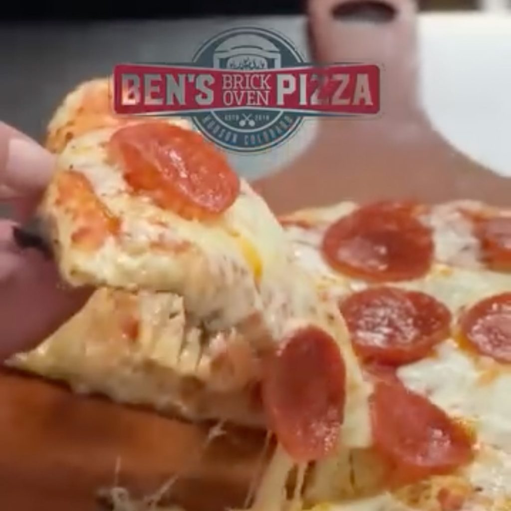 Still from a video showing the cheese pull from a slice of pizza being lifted from the pan