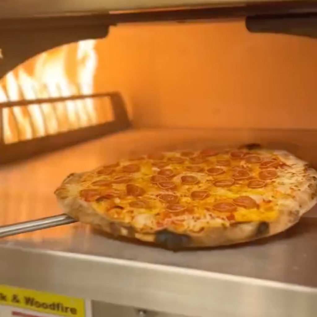 pulling a pizza out of a wood-fired oven